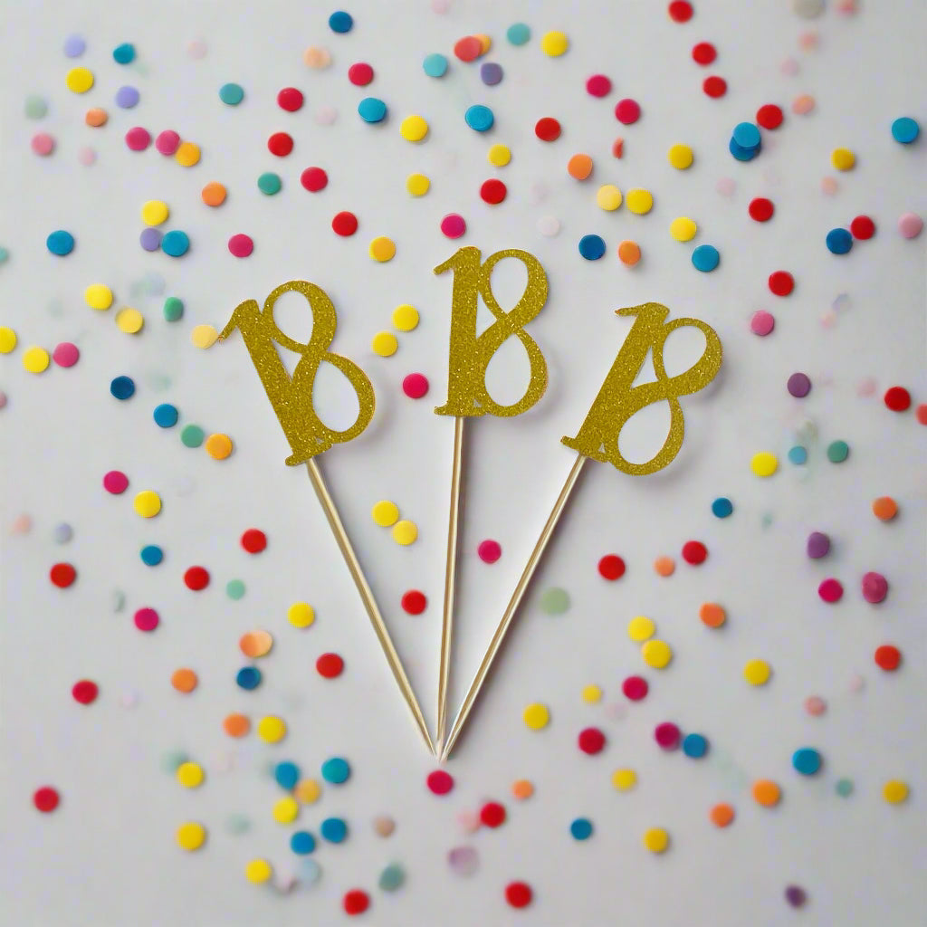 Three gold number 18 cake toppers on white background